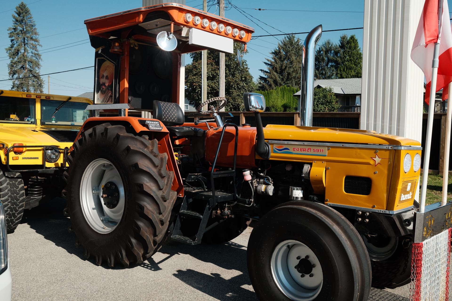 A Punjab show tractor in orange and yellow beside a yellow Hummer H1, parked together in the sun.